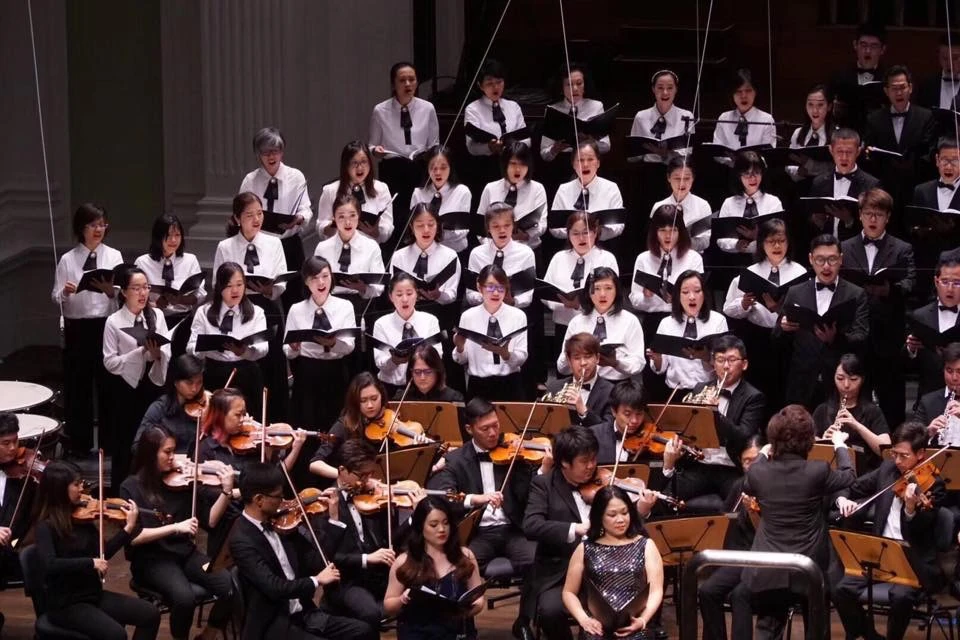 An orchestra and choir performing together, with string players, other instrumentalists and choir members visible.